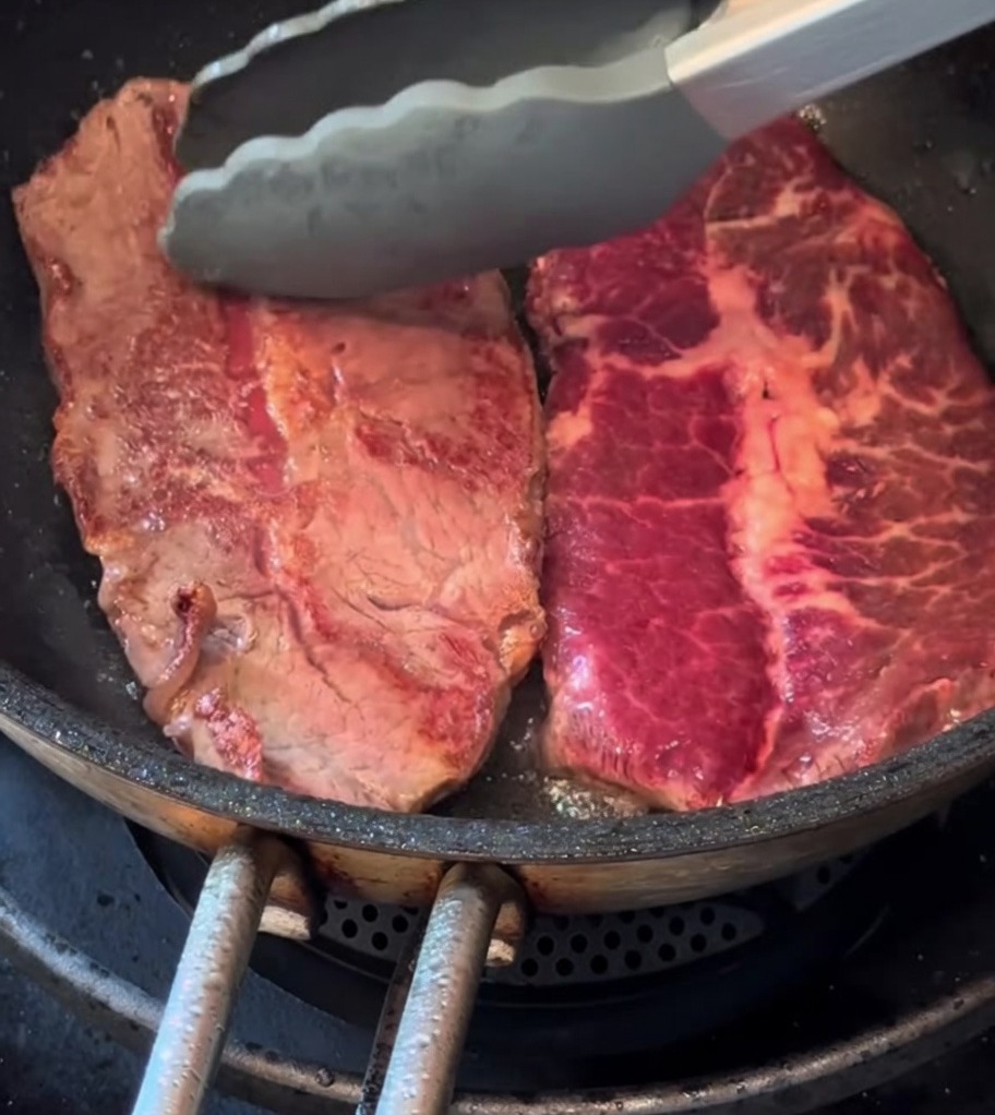 ローズマリーと一緒にフライパンで焼かれている薄切りステーキ。