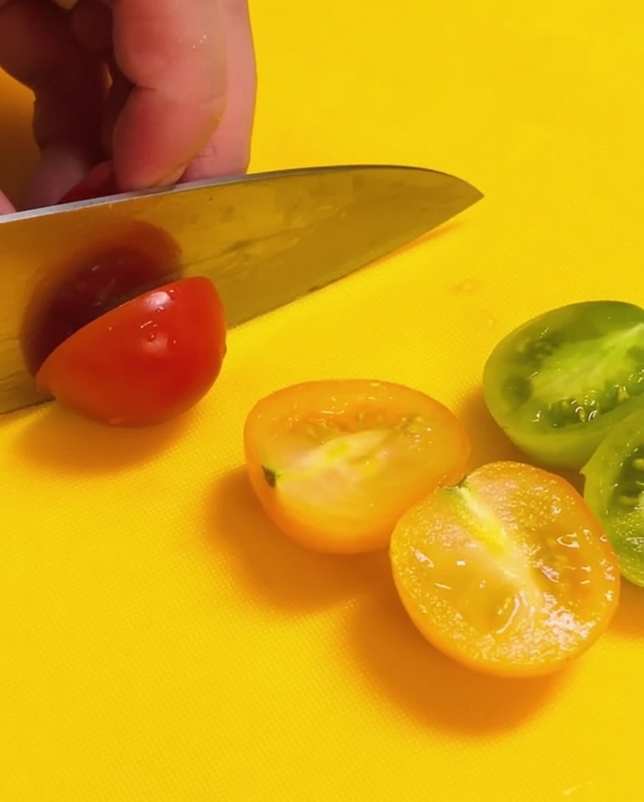 明るい黄色のまな板の上で、赤と緑のミニトマトを半分にカットしている様子。