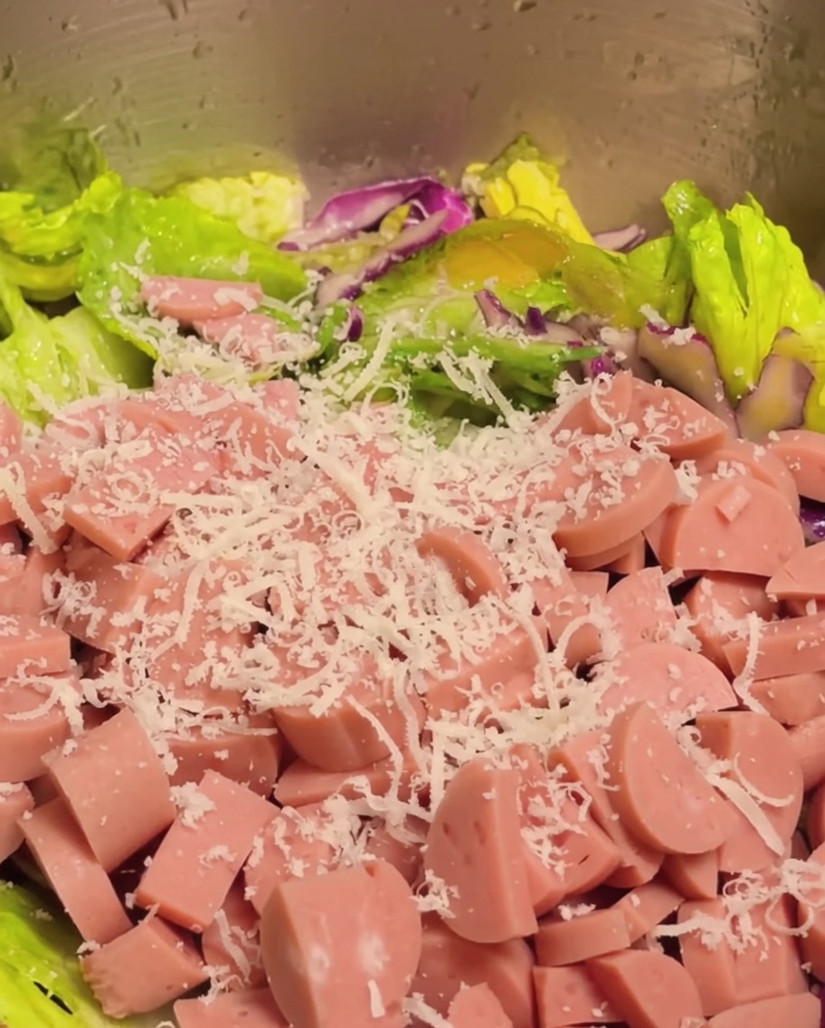 カットしたハムとおろしたパルメザンチーズを、ボウルの中の野菜サラダに加えている様子。