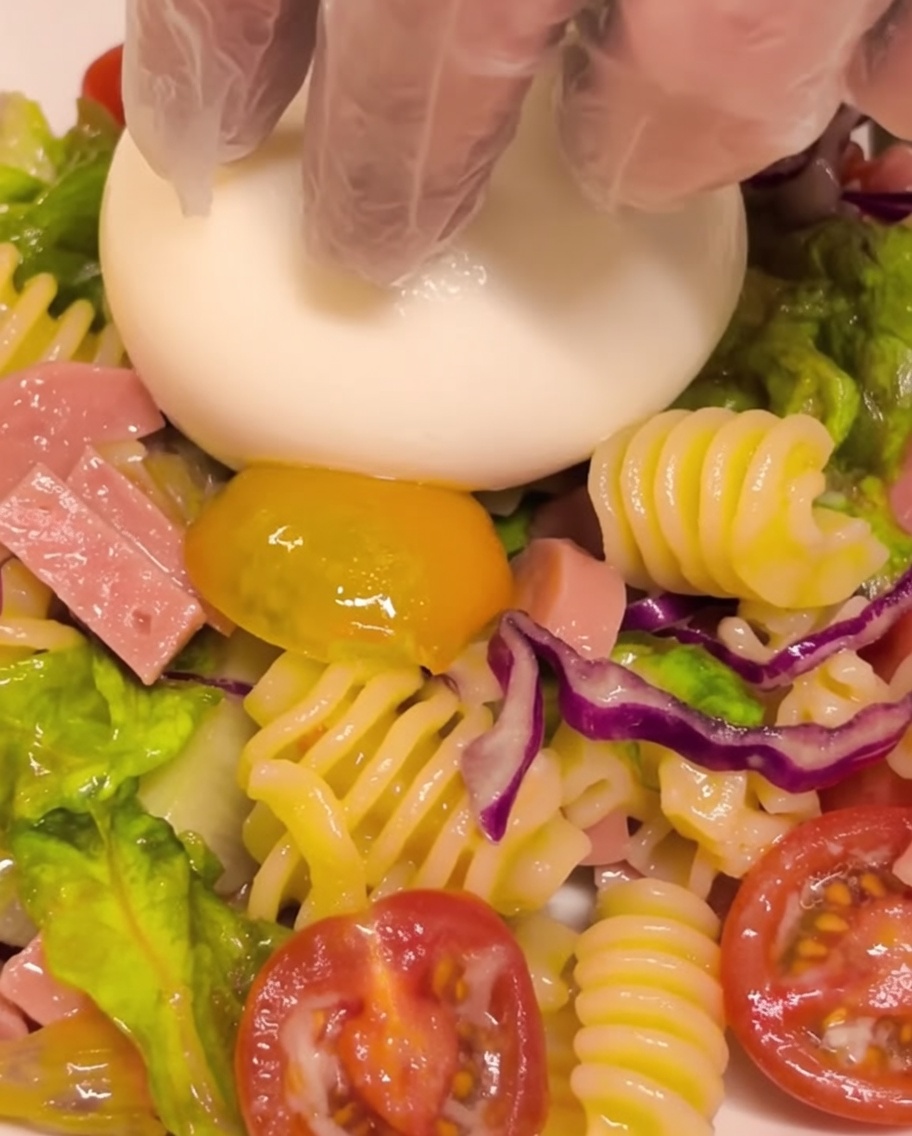 冷製パスタサラダの中央に、フレッシュなブラータチーズを丸ごと乗せている様子。