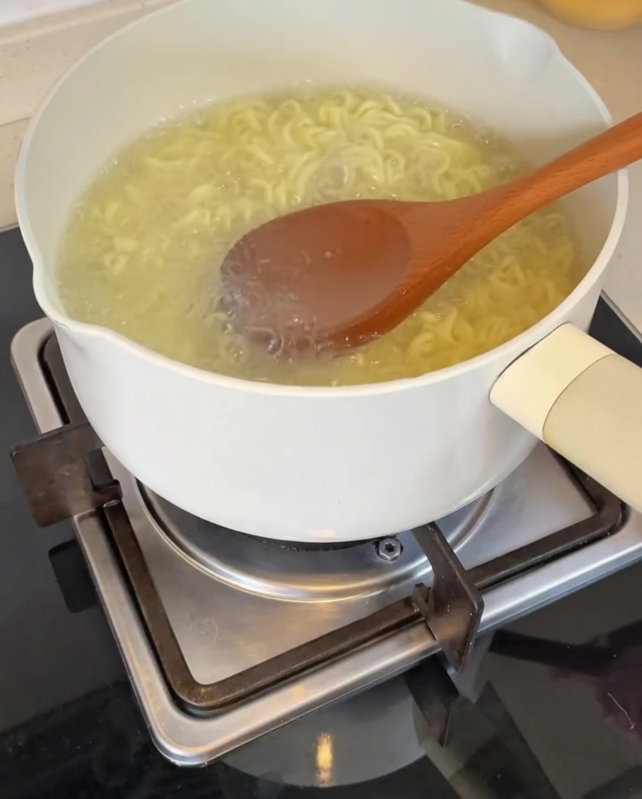お玉で熱い麺の茹で汁をボウルの中のタレに注いでいる様子。