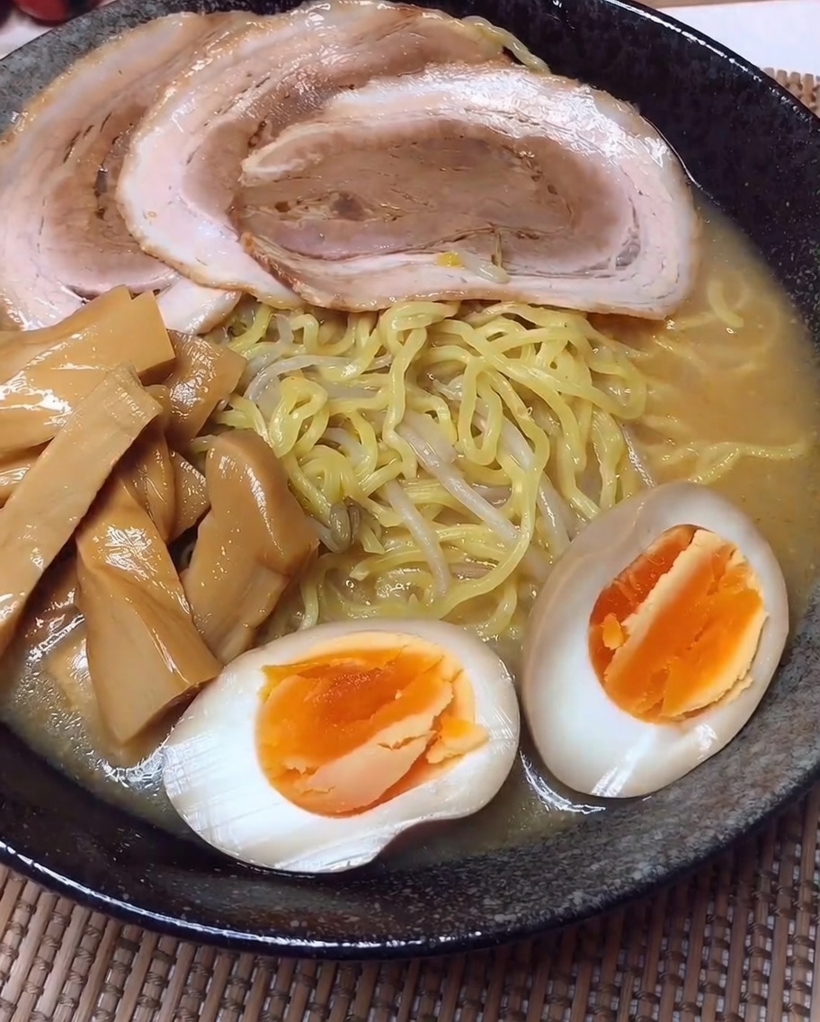 麺の上にチャーシュー、メンマ、卵を綺麗に盛り付けている様子。