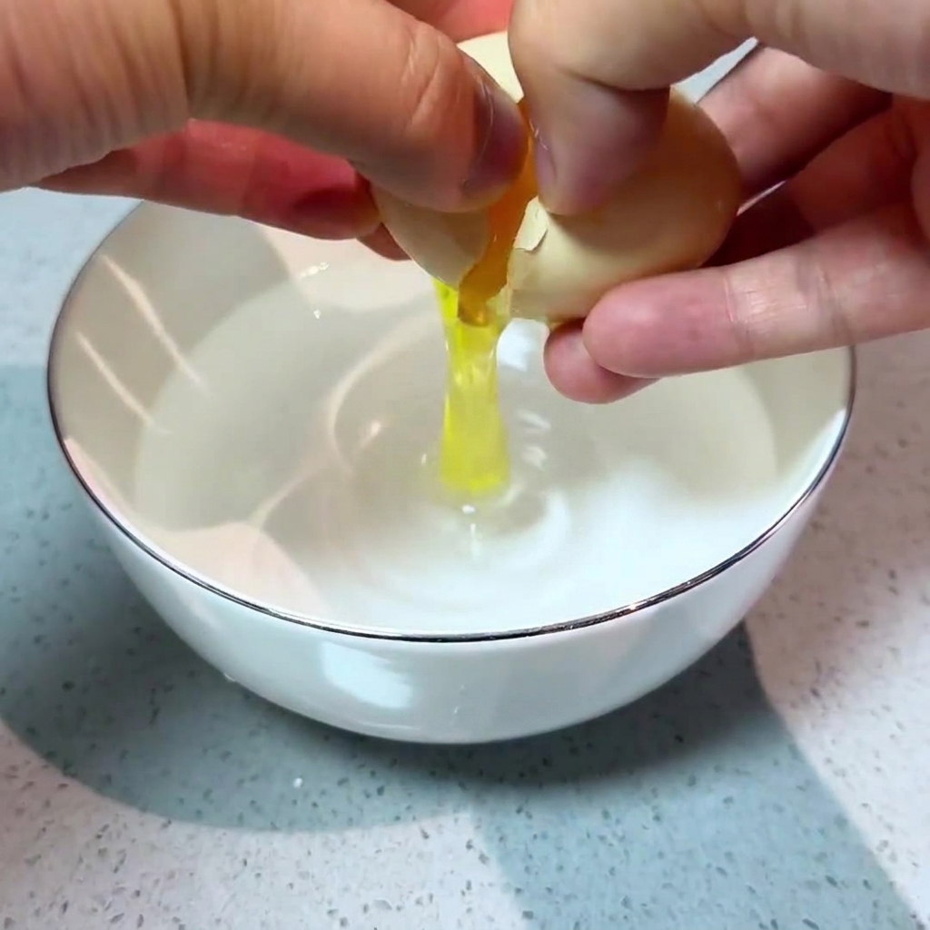 水を入れた小さな白い器に、卵を丁寧に割り入れる手元。