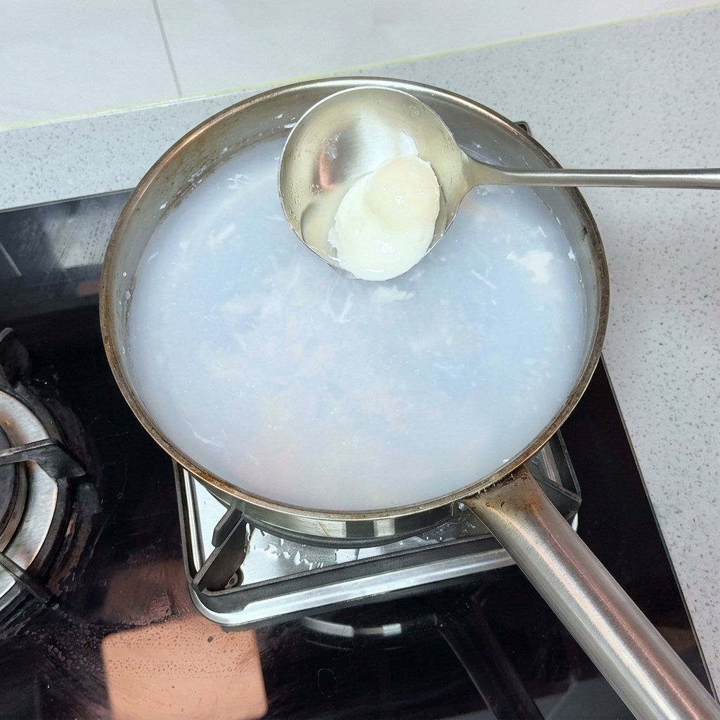 金属製のお玉で、鍋からポーチドエッグを慎重にすくい上げる様子。