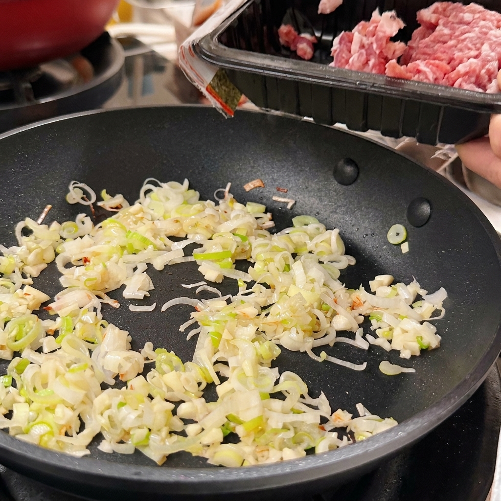 フライパンに入ったねぎとにんにくの横に、豚ひき肉を加えている様子。