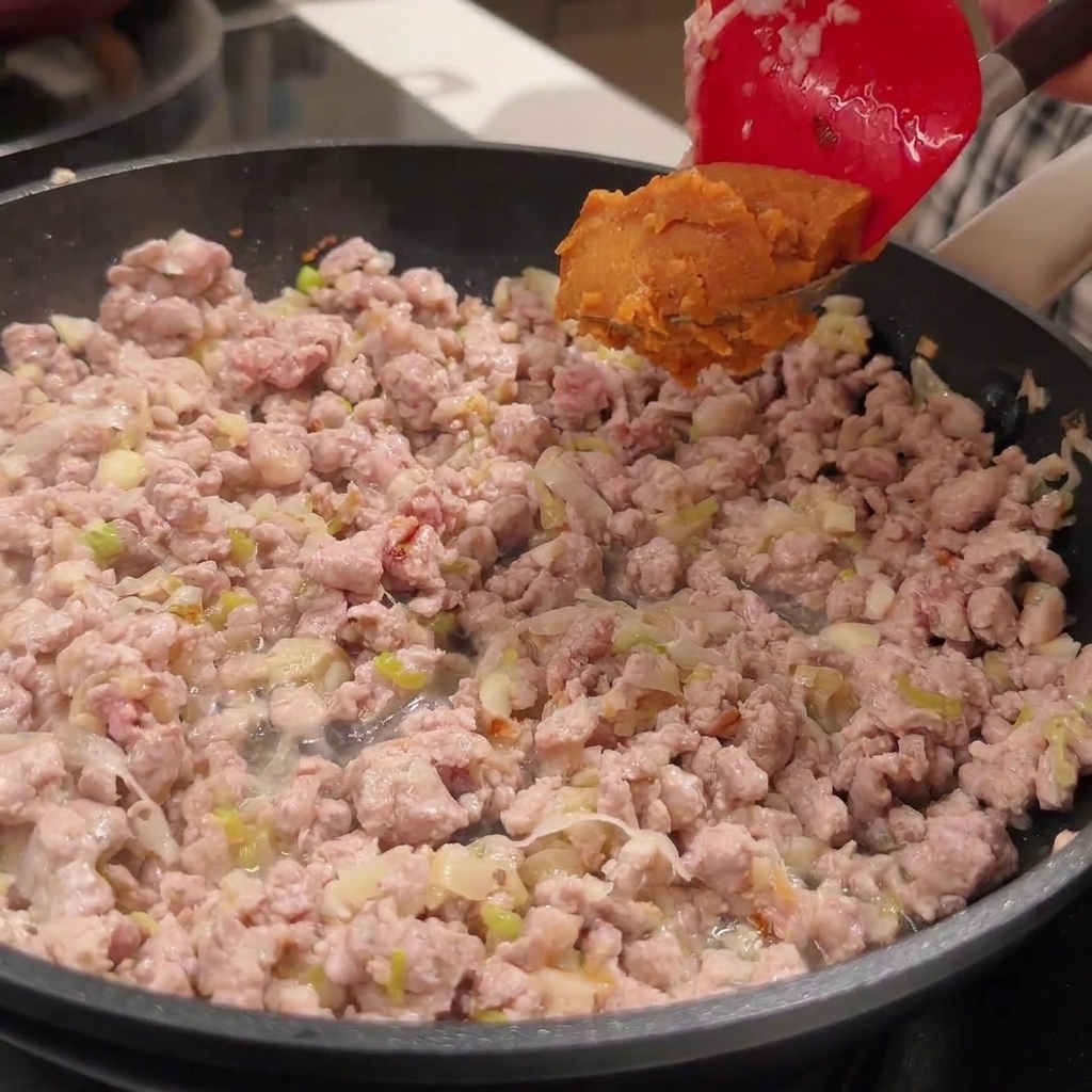 肉味噌のフライパンに、調味料を加えて混ぜ合わせている様子。