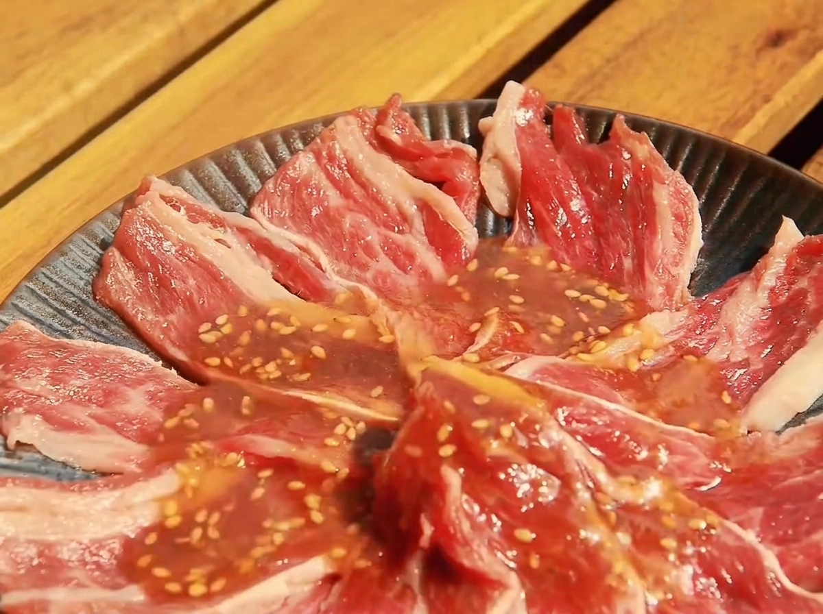 浅い容器に入れられた牛肉にタレをかけて漬け込んでいる様子。