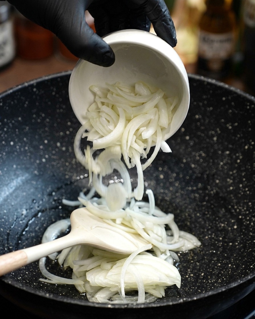 スライスした玉ねぎを熱した油に入れ、ヘラで炒めている様子。