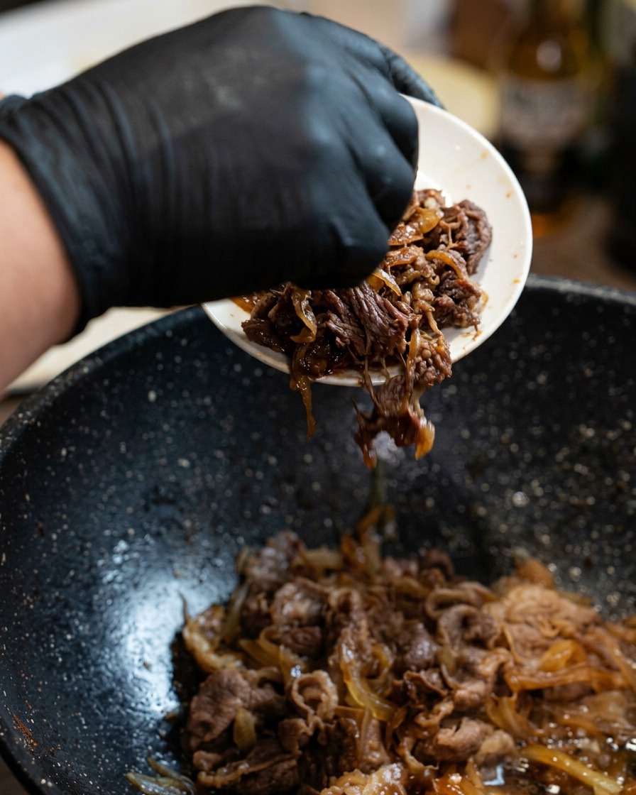 炊き立てご飯の上に、牛肉と玉ねぎの煮込みを盛り付けている様子。