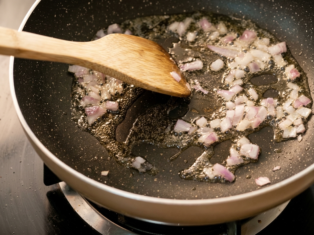 フライパンで油を熱し、みじん切りにした玉ねぎを木べらで炒めている様子。