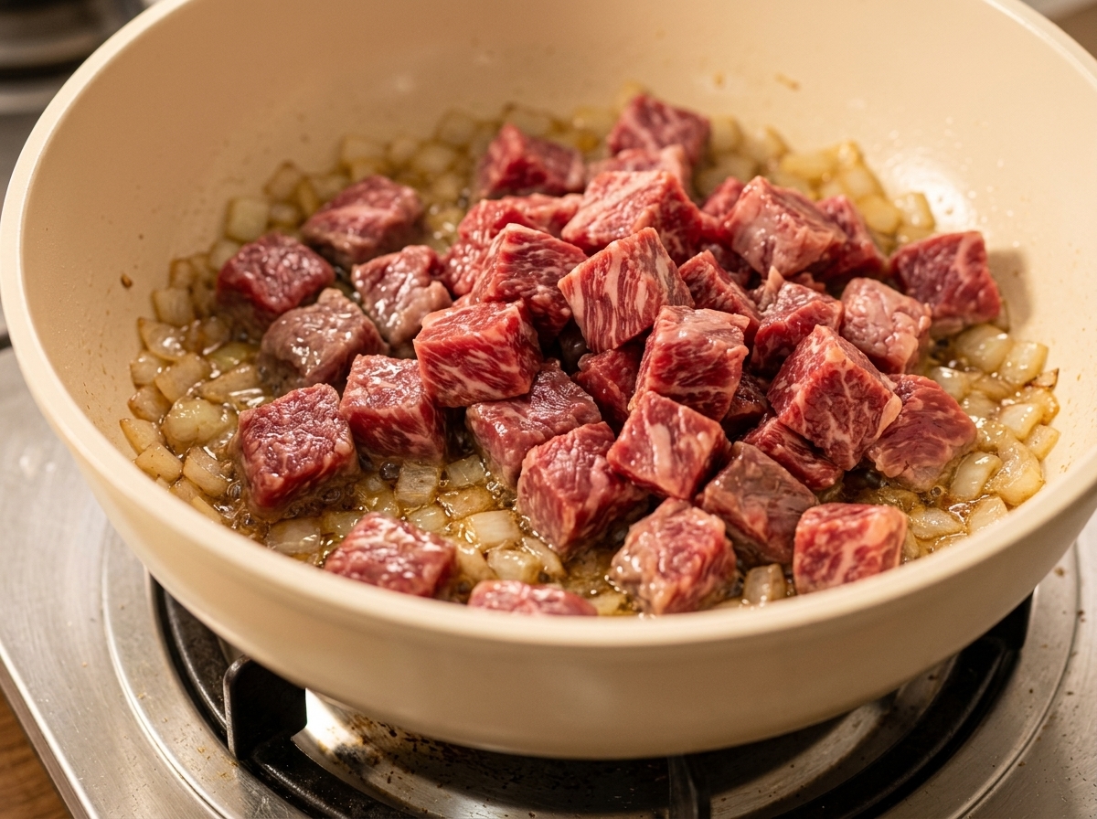 炒めた玉ねぎが入ったフライパンに牛肉と野菜を加え、混ぜている様子。