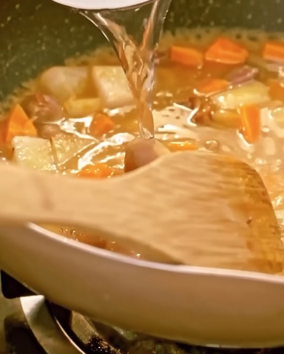 具材が浸るまで水を入れ、木べらで混ぜながら煮込んでいる様子。