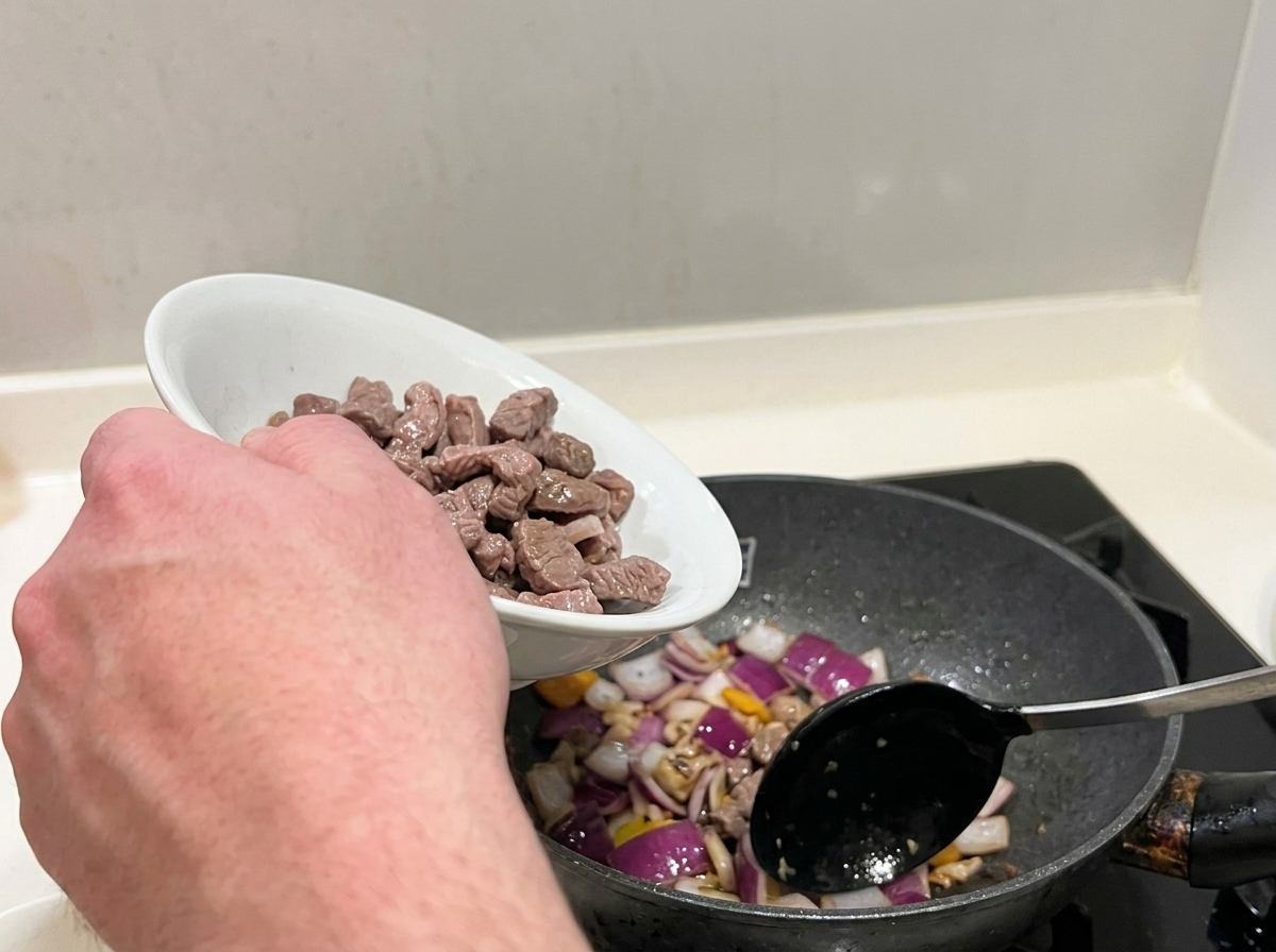 湯通しした牛肉と炒めた玉ねぎを合わせている様子