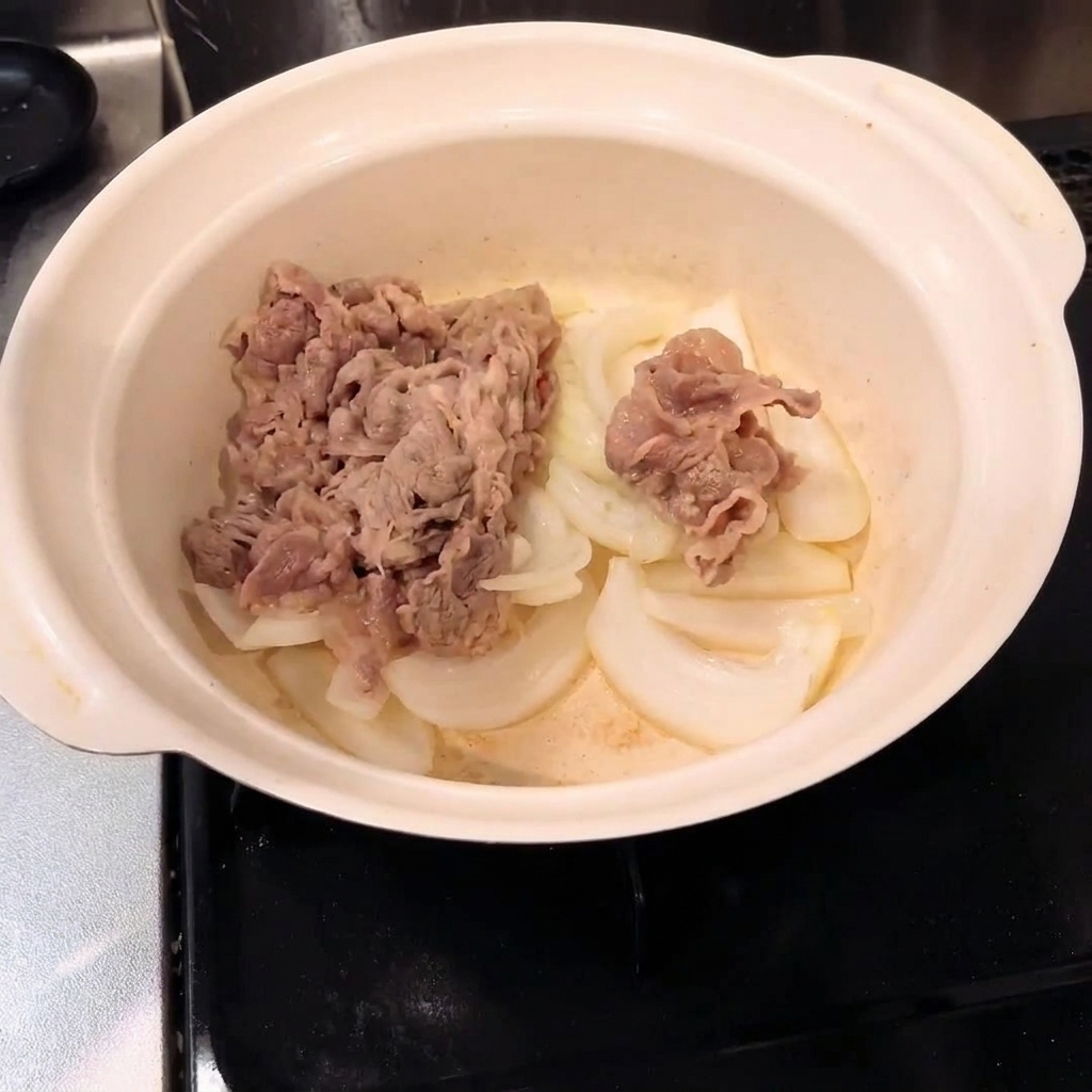 鍋の中で牛肉と玉ねぎを混ぜ合わせている様子。