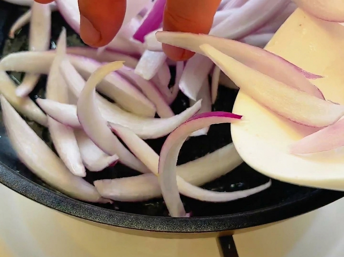 フライパンでスライスした赤玉ねぎを炒めている様子