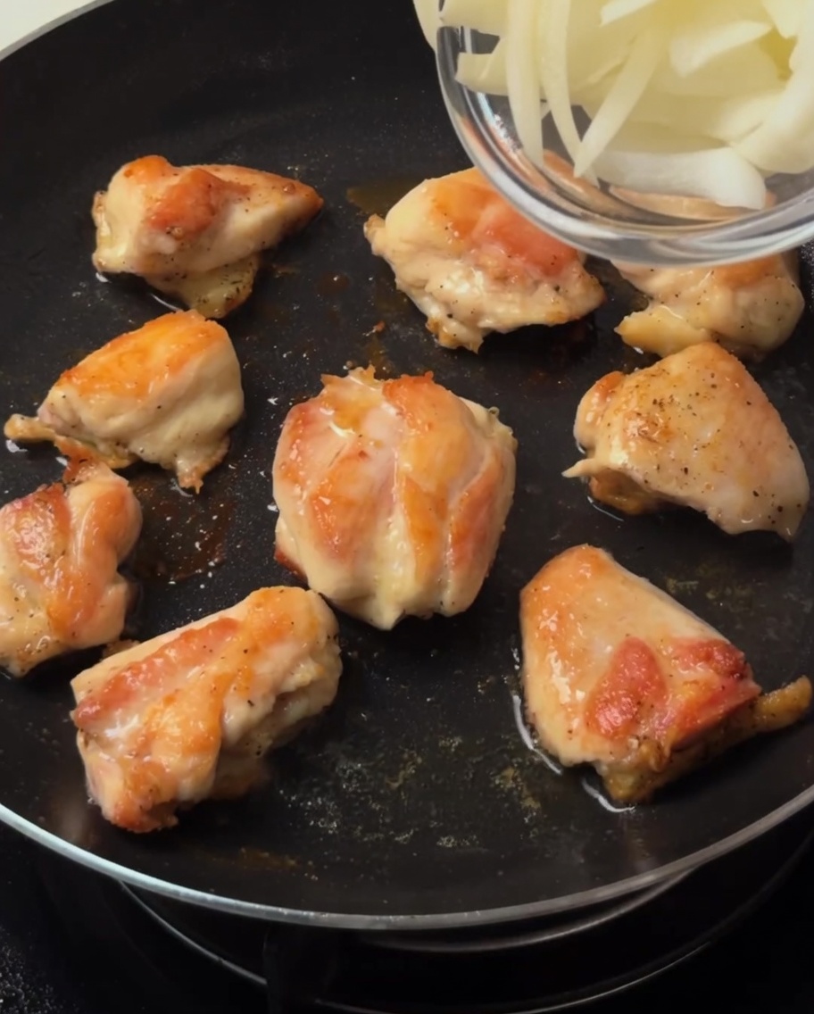 焼き目のついた鶏肉の入ったフライパンに、薄切りにした玉ねぎを加えて炒めている様子。