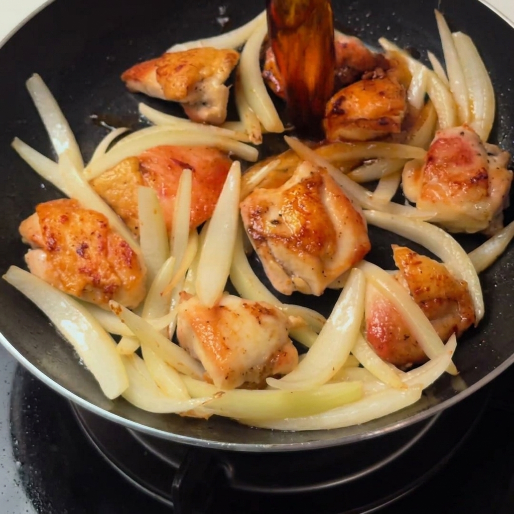 フライパンの中で、鶏肉と玉ねぎがだし汁ベースのつゆで煮込まれている様子。