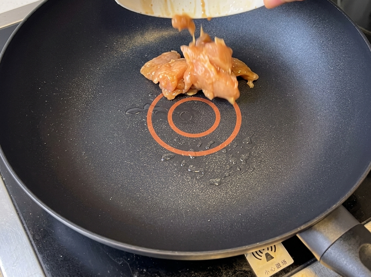 テフロン加工のフライパンでこんがりと炒められている鶏肉。