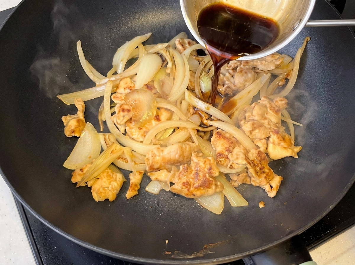 鶏肉と柔らかくなった玉ねぎの入ったフライパンに注がれるタレ。