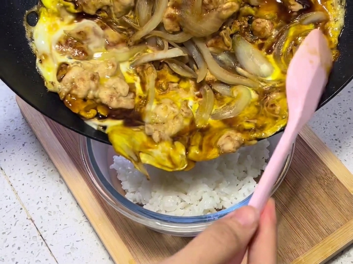 ほかほかのご飯が盛られた丼の上に、フライパンから具材をスライドさせて乗せている様子。