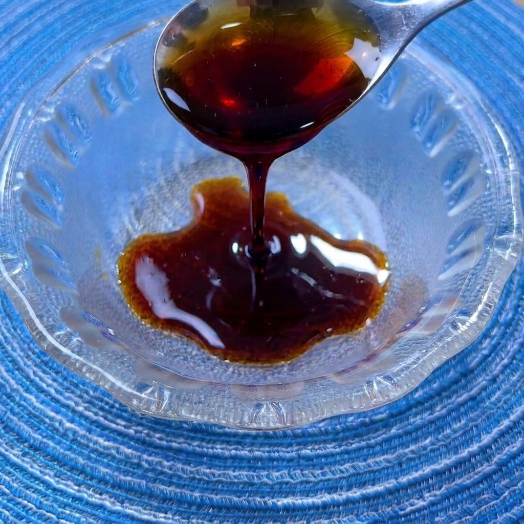 小さなガラスボウルで、醤油、オイスターソース、砂糖などの調味料を混ぜ合わせている様子。