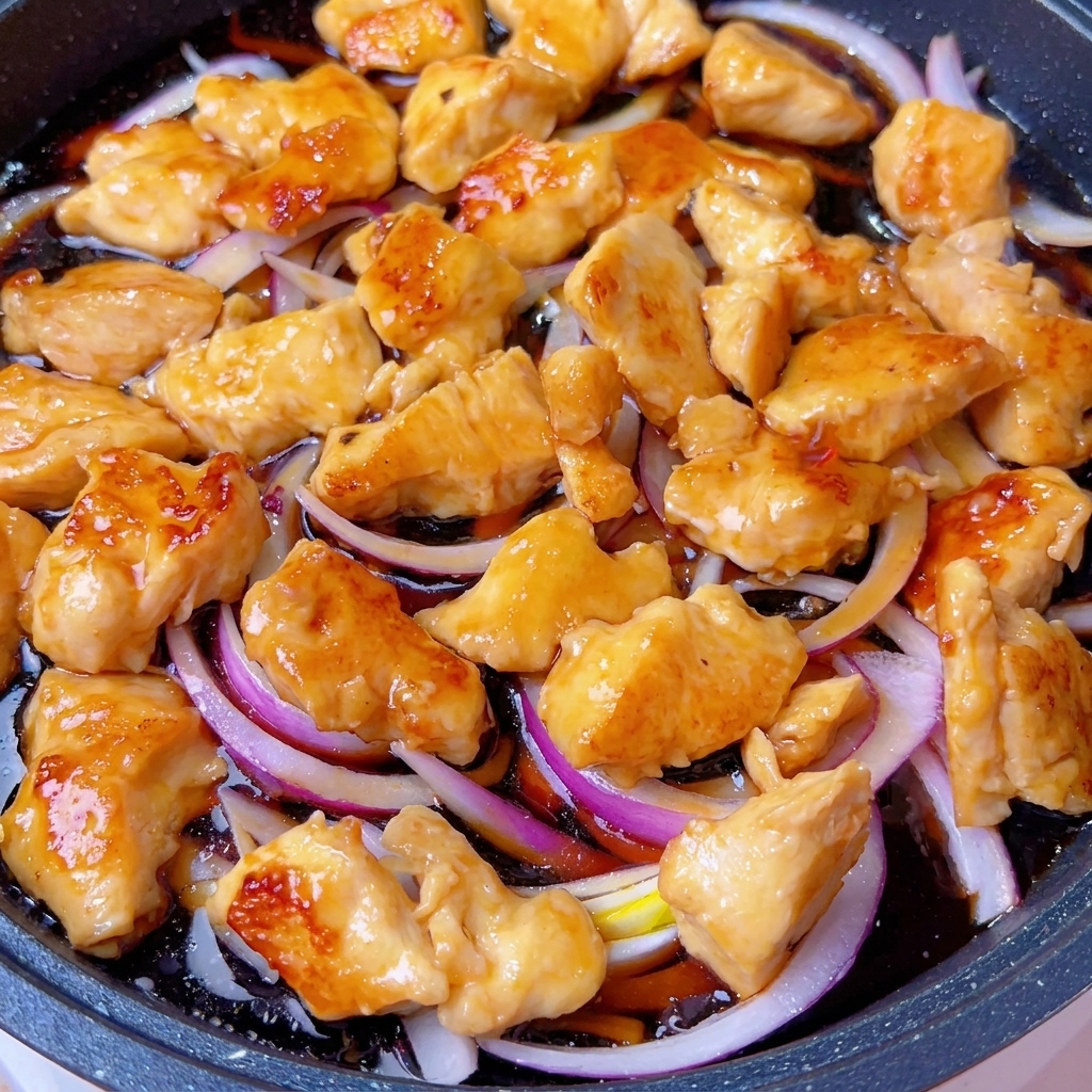 蓋をしたフライパンの中で、鶏肉と玉ねぎがグツグツと煮込まれている様子。