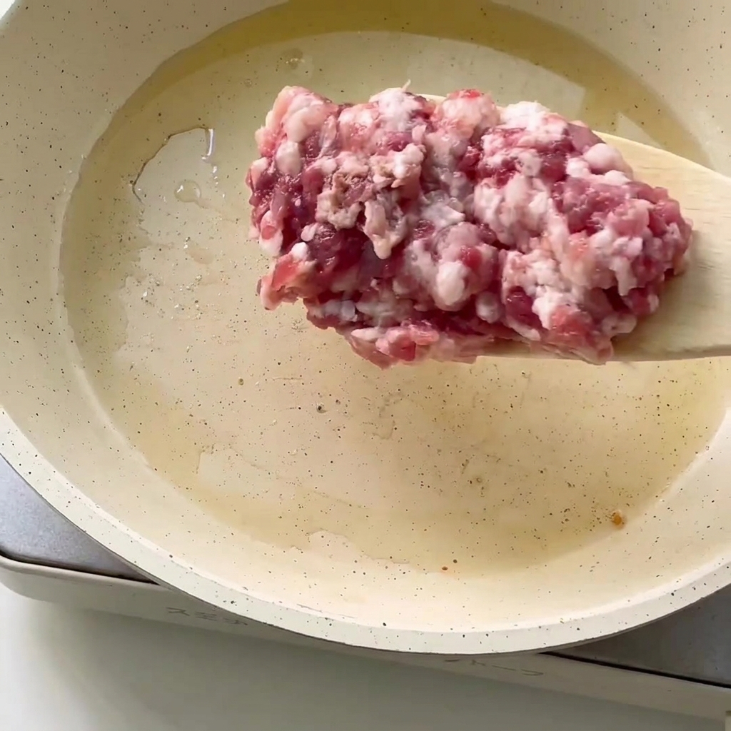 熱したフライパンに油をひき、ひき肉を入れる様子。