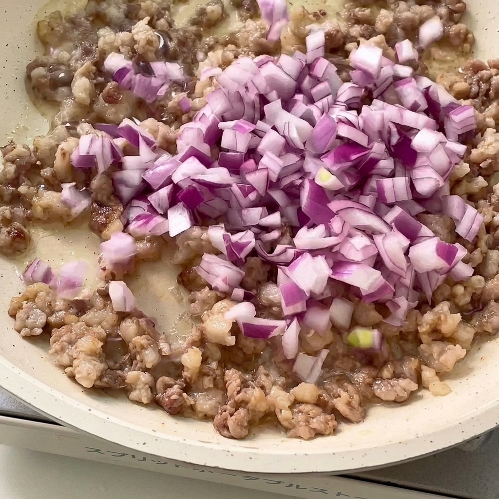 こんがり炒めたひき肉に、みじん切りにした赤玉ねぎとにんにくを加えて炒め合わせる。