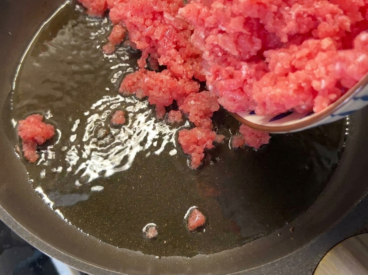 熱したフライパンにひき肉を入れる様子