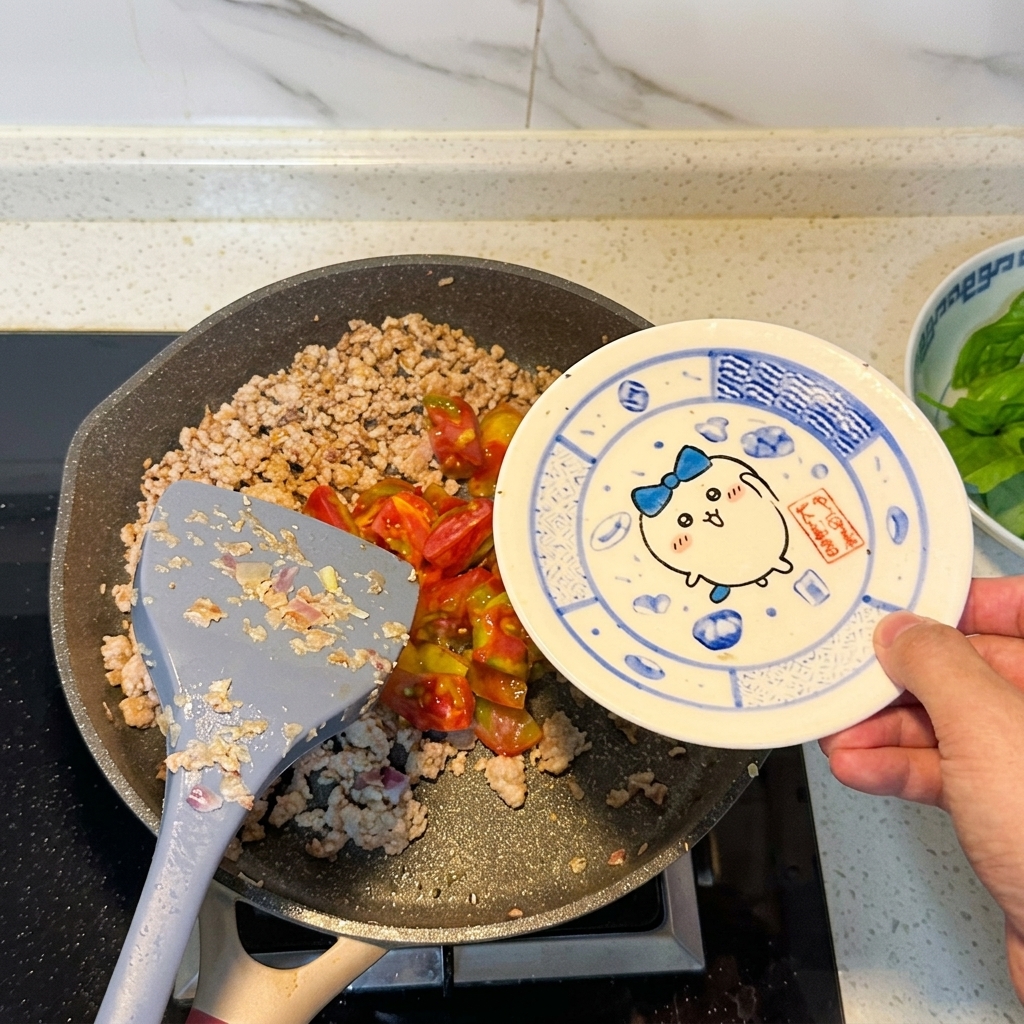 炒めた肉に刻んだトマトを加えている様子。