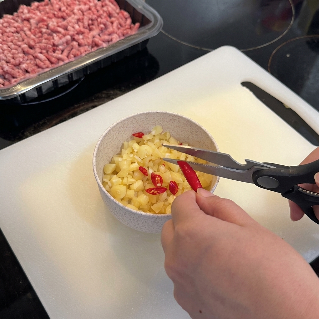 キッチンバサミで赤唐辛子をにんにくのボウルに切り入れている様子。