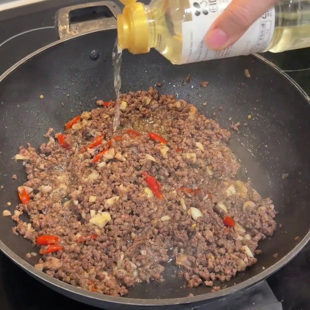炒めた肉に料理酒を振り入れている様子。