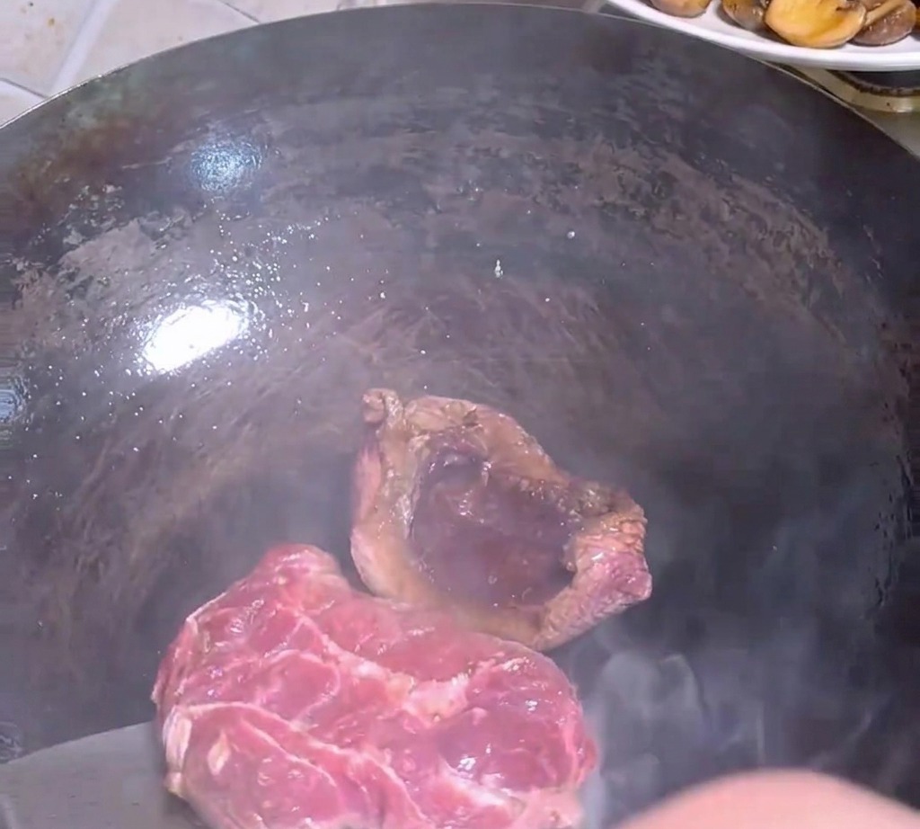 金属製のフライ返しで熱い鍋の中のステーキ肉を裏返している様子。