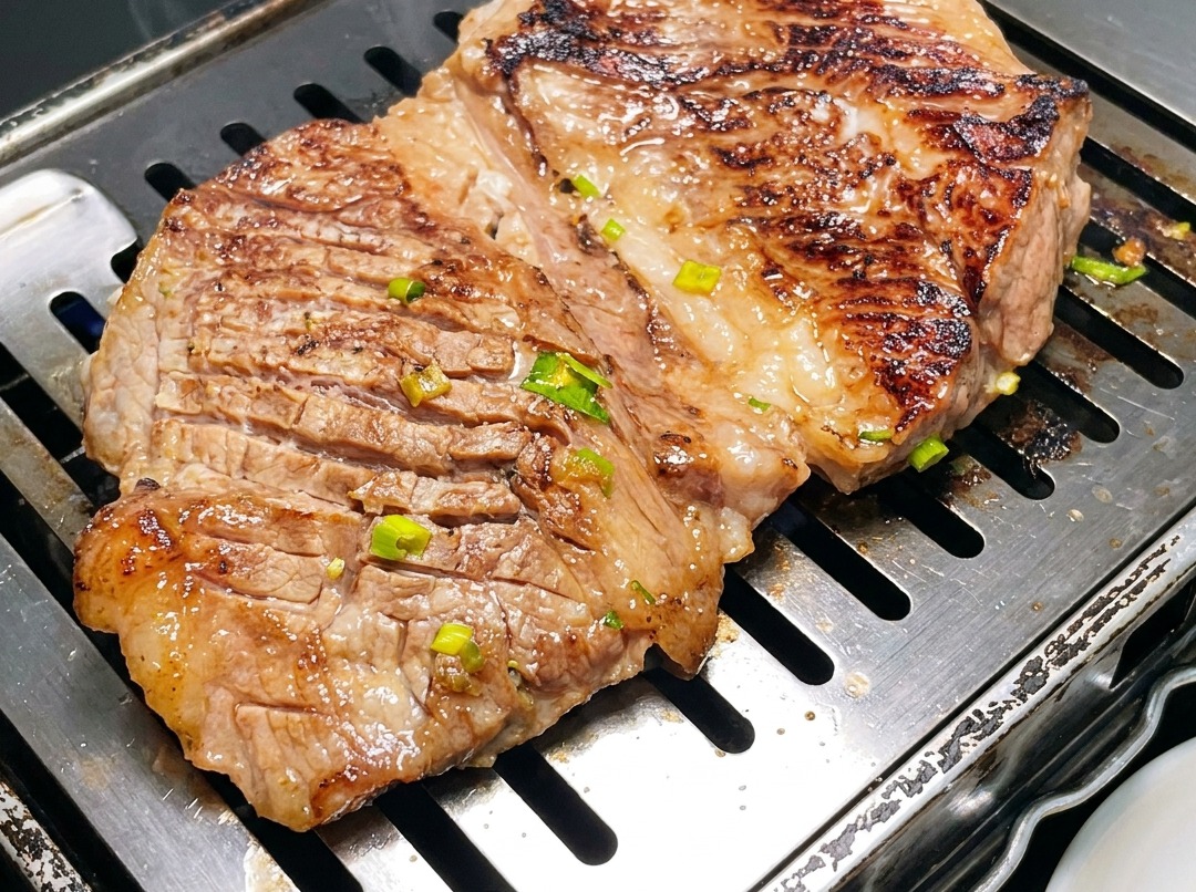 熱いグリルパンの上で、キッチンバサミを使って小さく切られている韓国風牛カルビ