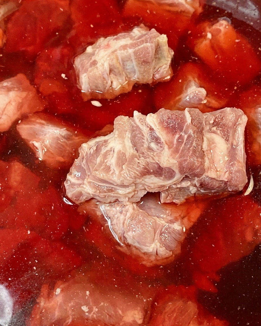 赤みがかった水が入ったボウルに浸された生の豚背骨。