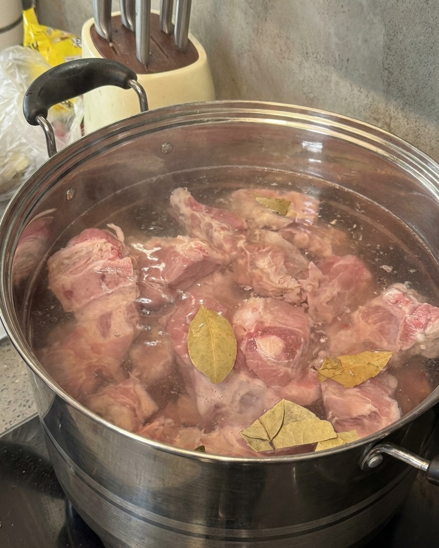 緑色のボトルから、豚骨とローリエが入った鍋に焼酎を注いでいる様子。