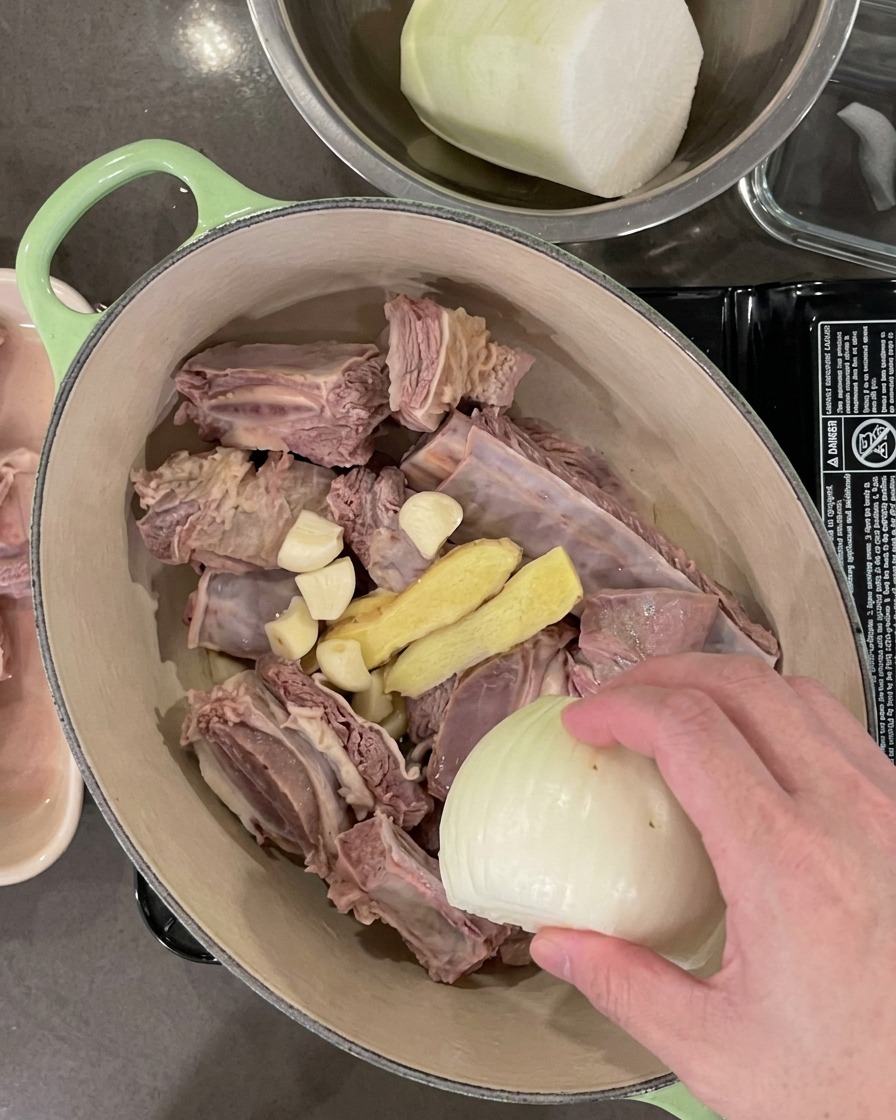 肉の入った鍋に、にんにく、生姜、玉ねぎ、長ねぎを投入している様子。