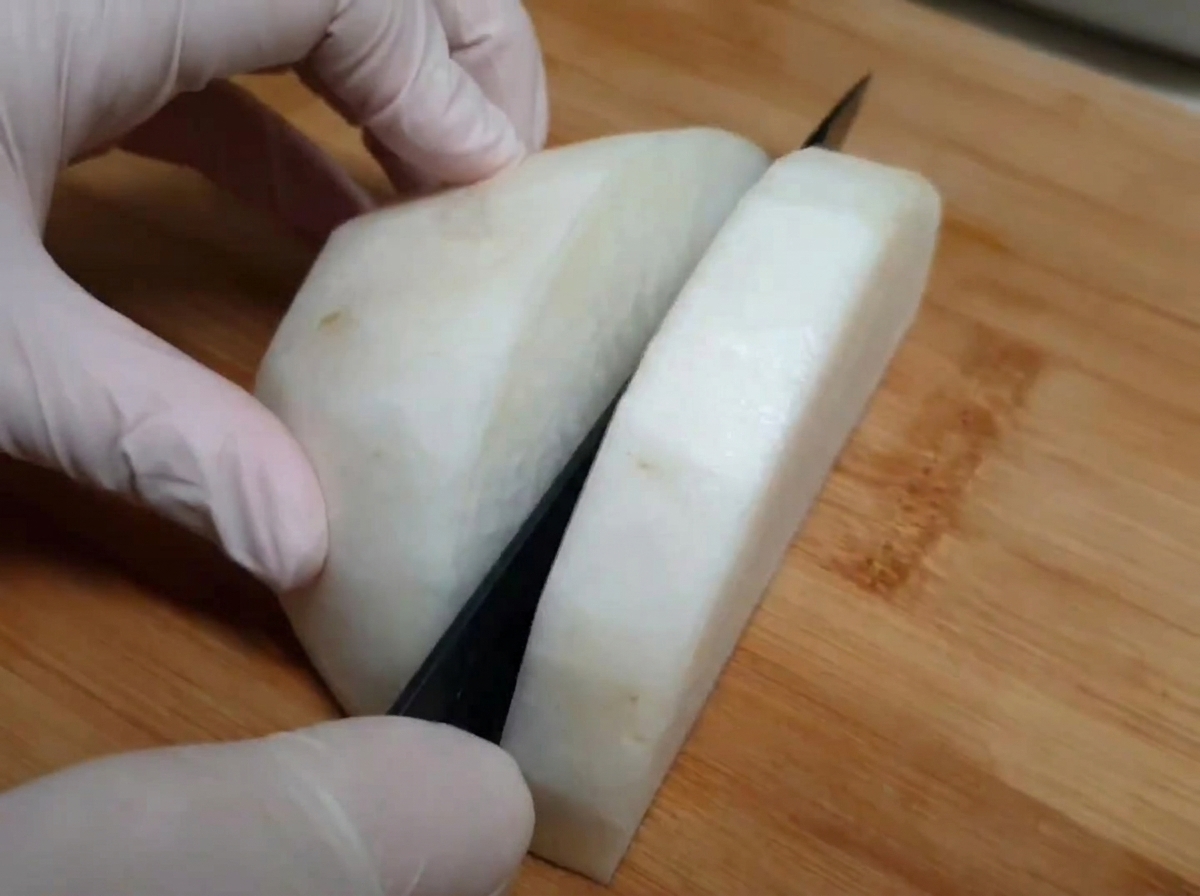 まな板の上で、料理用手袋をはめた手で大根を厚切りにしている様子。