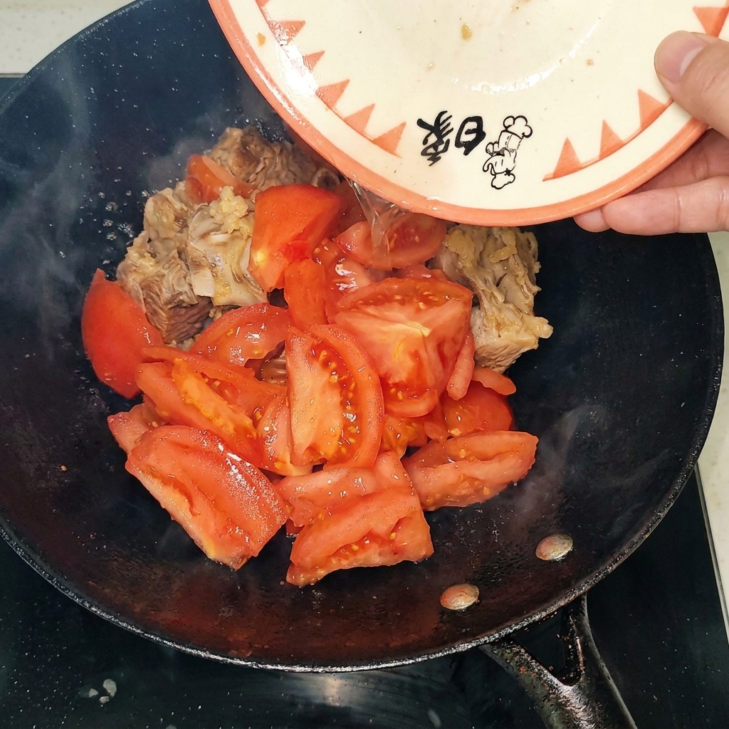 焼き色がついた牛スペアリブの入った中華鍋に、湯むきしてカットしたトマトを加えている様子。