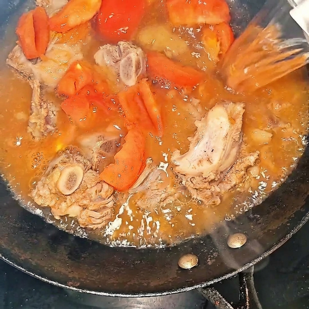 牛スペアリブとトマトが入った中華鍋に熱湯を注いでいる様子。