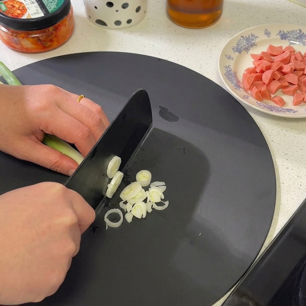 まな板の上で青ねぎの白い部分から緑の部分にかけて細かく刻んでいる様子。