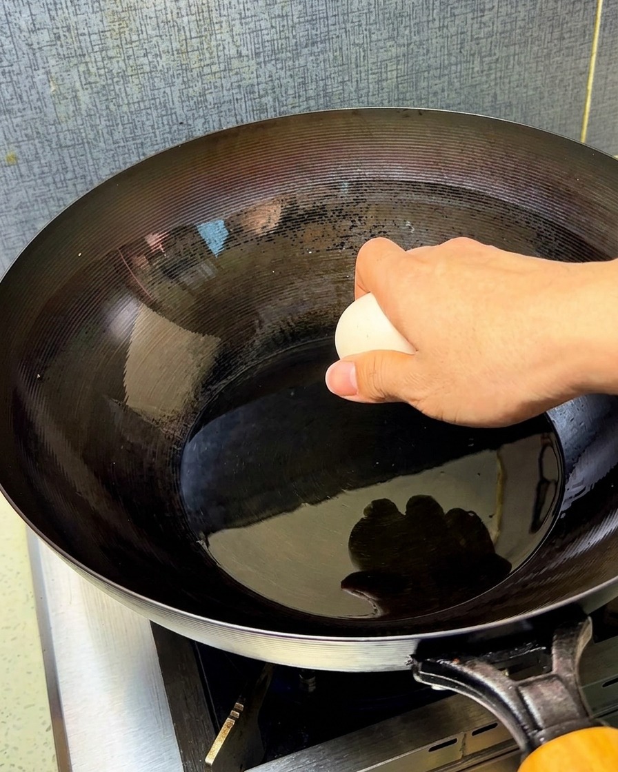 熱した中華鍋に油をひき、卵を割り入れる様子。