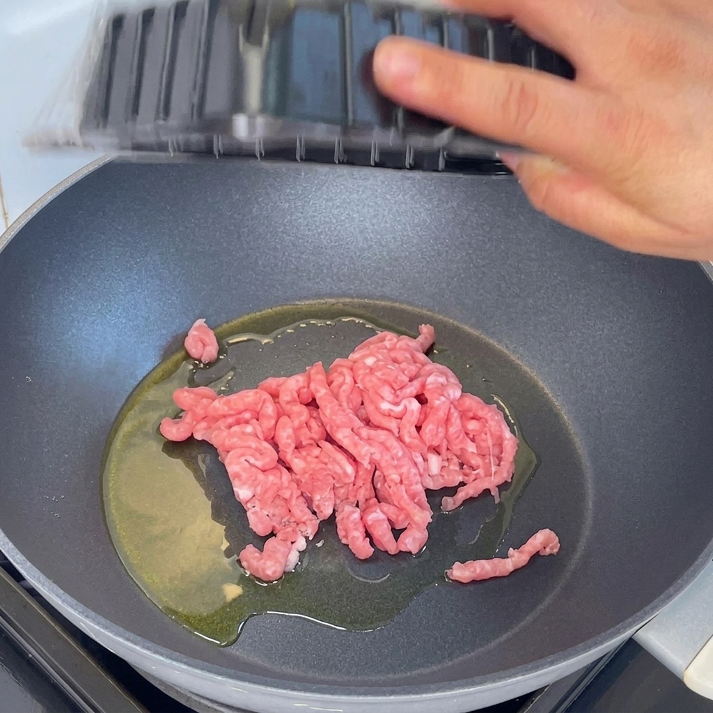 熱したフライパンに豚ひき肉を入れ、木べらで炒めている様子。