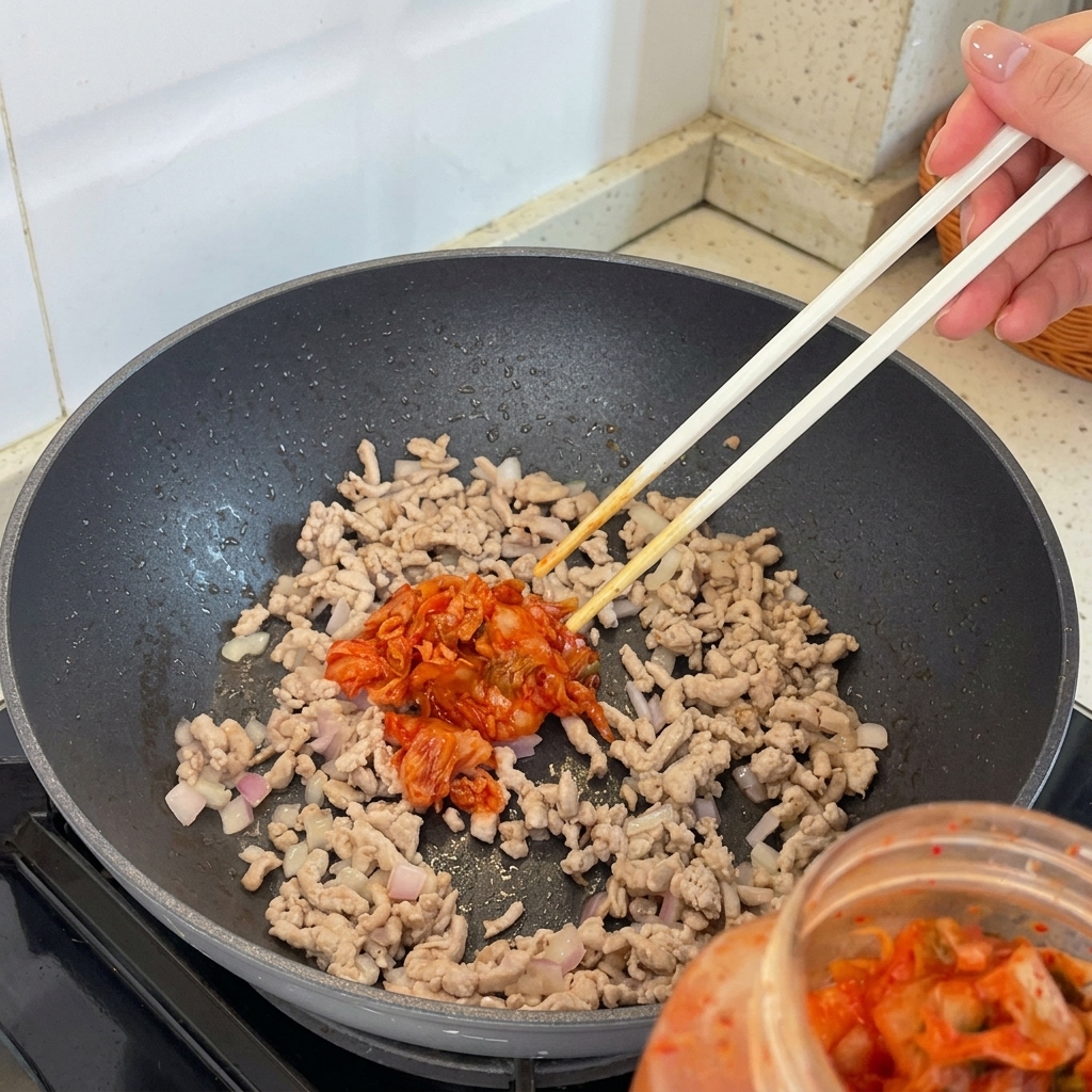 豚肉とエシャロットを炒めたフライパンにキムチを加えている様子。