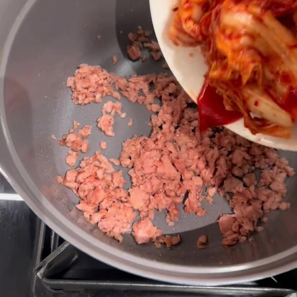 炒めたスパムの入った鍋にキムチを加えて炒めている様子。