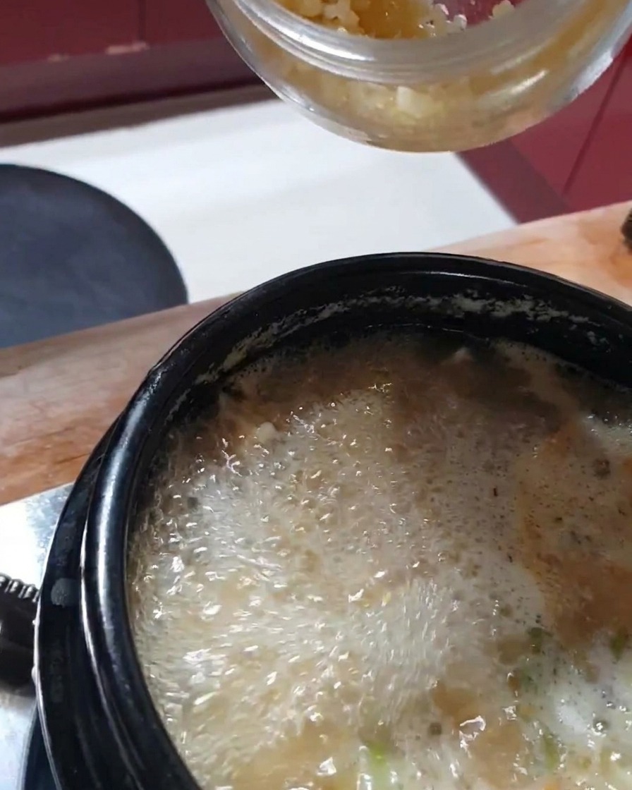 ぐつぐつ煮えるチゲにすりおろしにんにくを加えている様子。