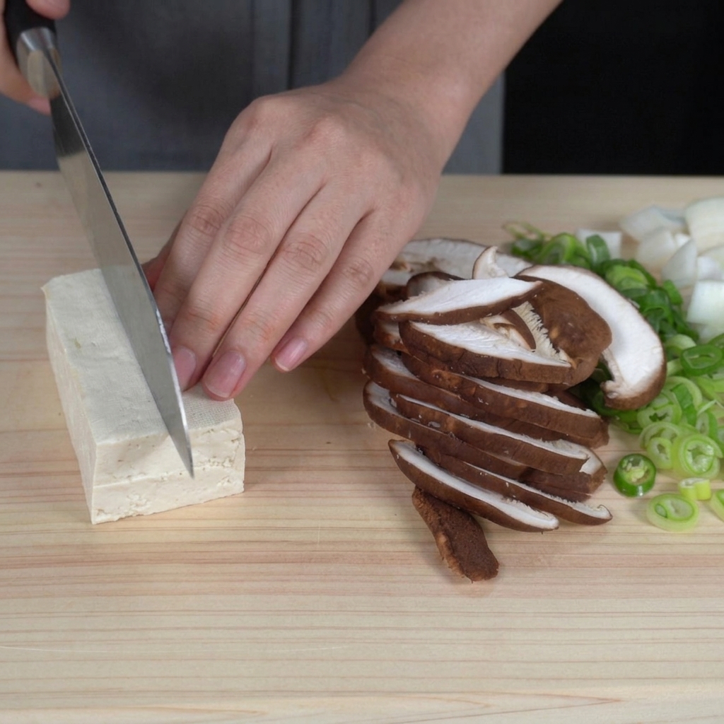 木綿豆腐をまな板の上で一口サイズに切っている手。