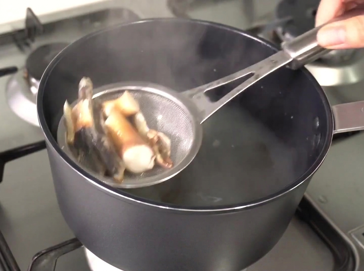 金属製のザルを使って出汁から煮干しと昆布を取り出している様子。
