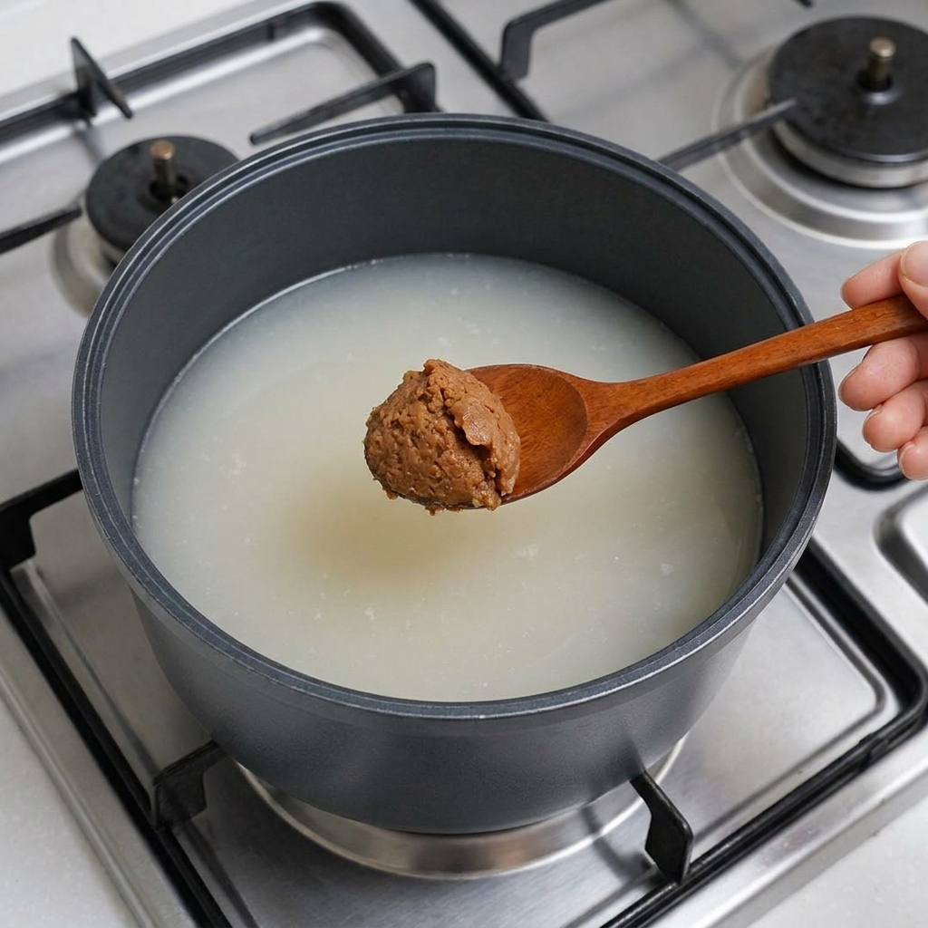 木製のスプーンで味噌をスープに溶かし入れている様子。