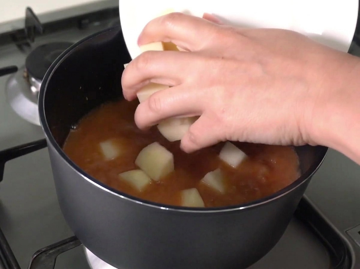 切ったジャガイモと玉ねぎを沸騰したスープに入れている様子。